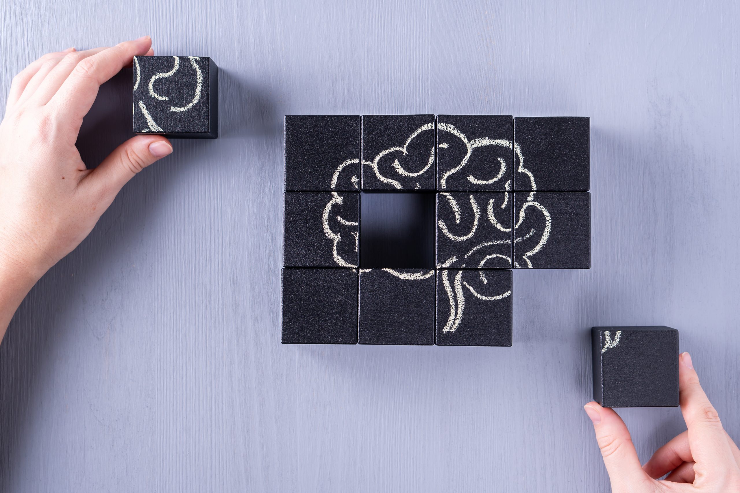 <p>The concept of the human brain. Education, science and medical concept.  Brain drawn in chalk on black cubes.<br />
Female hands put in place the last element of the puzzle.</p>
