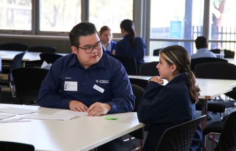A male university student talking to a younger female high school student