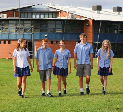 Five students smiling and walking on the grass