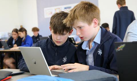 Two male students looking at a laptop in a classroom